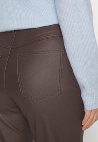Brune faux læderbukser med en struktureret overflade, der har en enkelt baglomme og brune sømme, parret med en lyseblå strikket sweater.