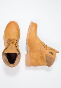 Botines tobilleros marrones hechos de cuero suave y ante, con punta redonda, diseño de cordones y suela de goma texturizada con estrías.