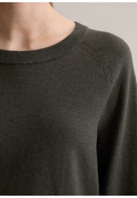 Mörkgrön stickad tröja med rund halsringning, raglanärmar och en mjuk textur. Tyget verkar något fluffigt med en slät finish.