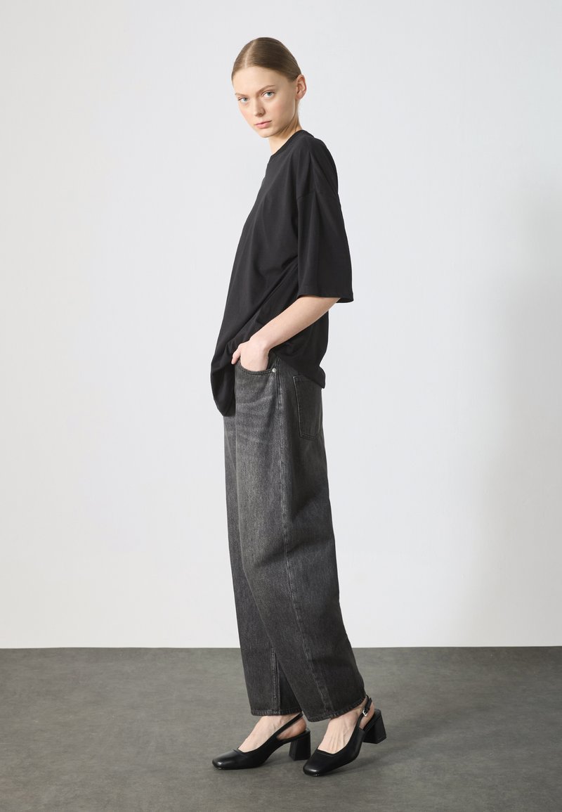 Maglietta nera over-size, pantaloni in denim grigio larghi, e scarpe con tacco nere. Tessuto morbido, vestibilità rilassata e silhouette definita.