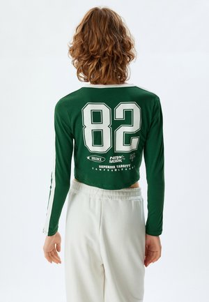 Green long-sleeve crop top with white accents, featuring the number "82" and text at the back, made from a smooth, stretchy fabric.