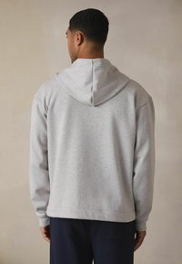 Jasnoszara bluza z kapturem, wykonana z miękkiego materiału w luźnym fasonie. Posiada regulowany kaptur, prążkowane mankiety oraz wykończenie dołu, co zapewnia lepszy komfort.