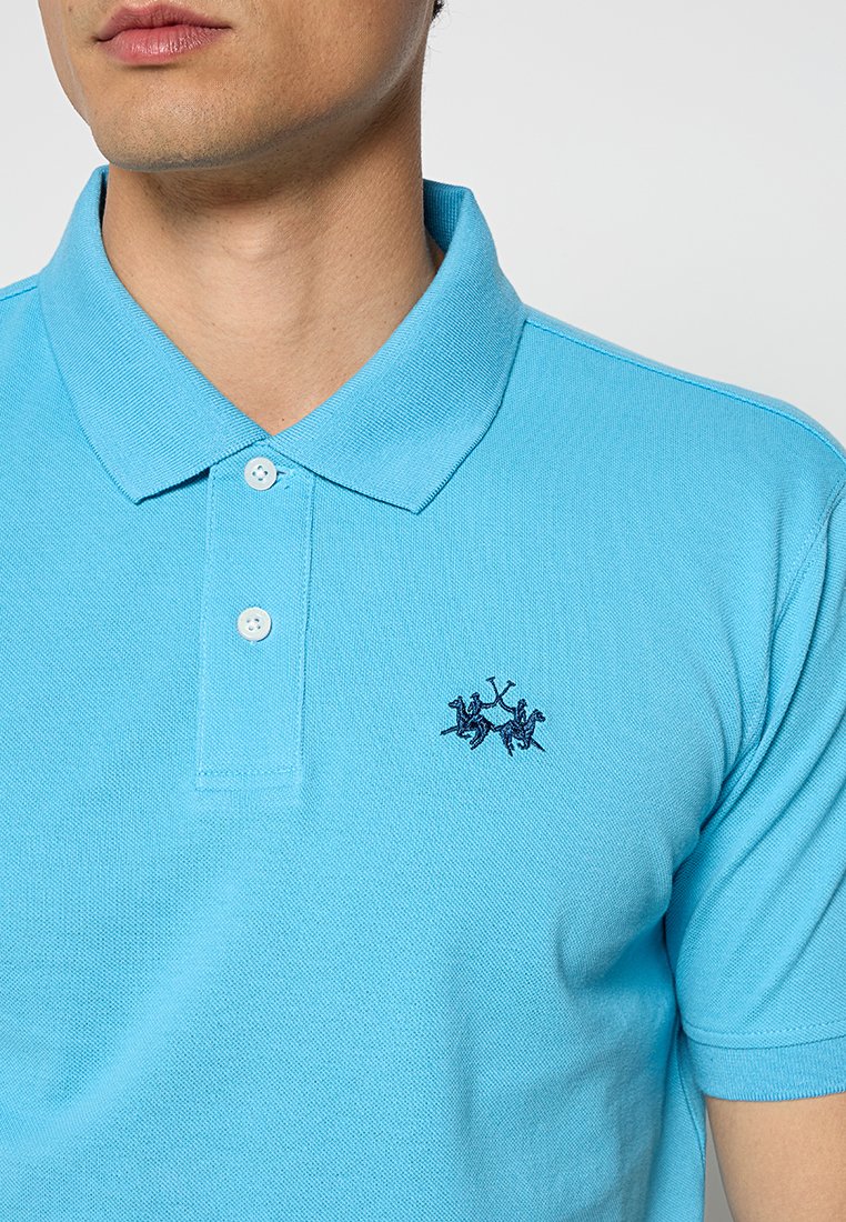 Lichtblauwe poloshirt van textuur katoen met een klassieke kraag, voorzien van twee knopen en een geborduurd embleem in marineblauw.