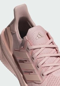 Adidas Ultraboost-sko i lys rosa med en teksturert overdel, snøring og tre horisontale striper på siden.