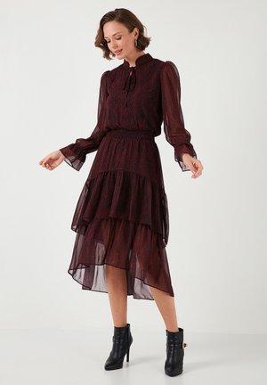 Robe à motifs rouge et noir avec un ourlet volanté et des manches longues, assortie à des bottines noires, présentant un col à nouer et un tissu transparent.