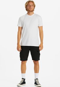 Hvid kortærmet T-shirt, sorte cargo shorts, hvide ankelstrømper og sorte højhælede sneakers. Enkel, afslappet påklædning med lommer.