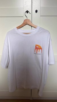 Hvid bomuld T-shirt vist på en træbøjle med en orange stol grafik og tekst i nederste højre hjørne.