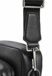 Bolso de cuero negro con superficie texturizada, que presenta un clip y una correa de metal plateado. Detalle de cremallera visible en el lateral para acceso al cierre.