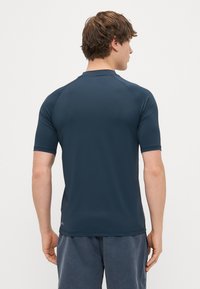 Marinblå kortärmad atletisk tröja med en åtsittande design, slät struktur och platta sömmar. Bakifrån visas raglansärmar och detaljer vid fållen.