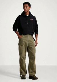 Svart hettegenser med logo, olivengrønne cargo-bukser og mørke sko. Bukserne har sidelommer og en avslappet passform.