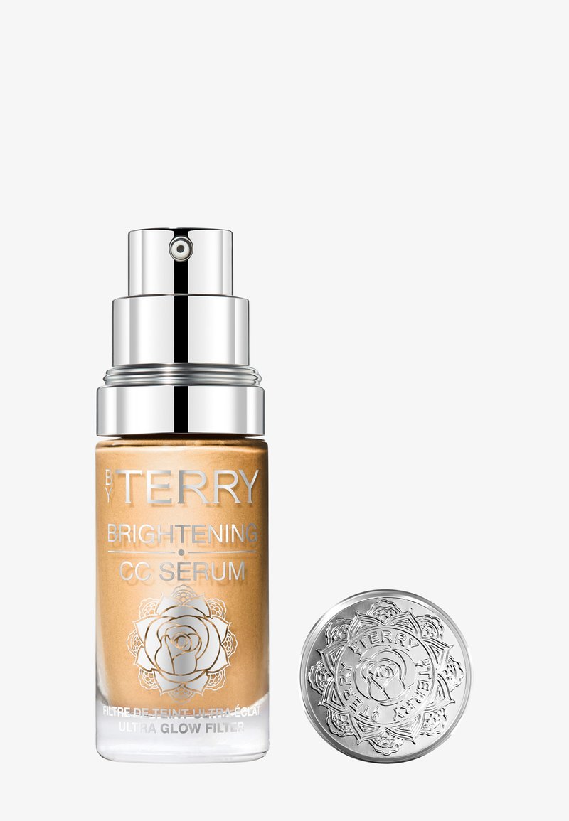 Flacon de sérum CC éclaircissant avec distributeur à pompe et bouchon décoratif argenté, étiqueté "By Terry Ultra Glow Filter" sur fond blanc.