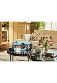 Couchtisch mit einer schwarz-weiß gestreiften Tischplatte, dekorativen Kästchen, Kerzen und einer Glasvase mit bunten Tulpen.