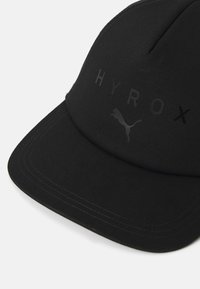 Black cap made of fabric, featuring a curved visor, embossed "HYROX" text, and a small Puma logo in a dark tone. Smooth texture.