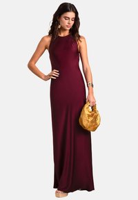 Abito da sera bordeaux in tessuto liscio con silhouette aderente, design senza maniche e lunghezza alla caviglia. Gli accessori includono una borsa in oro con texture.