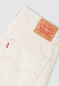Offwhite Levi's denimjeans som visar bakficka med röd flik och brunt lädermärke märkt W 32 L 32, stil 578.