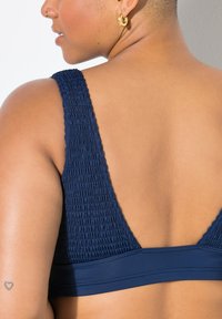 Námořnická modrá podprsenka s nařasenou texturou a širokými ramínky, s hladkým pásem na spodní straně a nízkým designem zad.