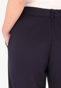 Pantaloni blu navy con una texture liscia, dotati di una vita piatta, tasche e una vestibilità su misura, che mettono in risalto un design pulito e minimalista.