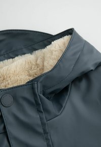 Ciemnoszara kurtka z kołnierzem, wykończona miękkim beżowym futerkiem typu 'fake fur'. Posiada gładką powierzchnię, przeszycia oraz mały akcent w postaci logo.