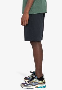 Schwarze Baumwollshorts mit einem schlichten Design, kombiniert mit mehrfarbigen Sportschuhen, die über Netz- und Texturakzente verfügen.