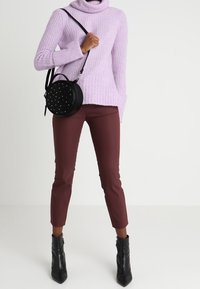 Light purple knit turtleneck sweater, fitted maroon ankle pants, black ankle boots with a shiny finish, and a round black bag with studs.