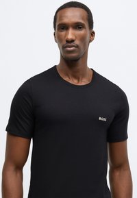 T-shirt nera a maniche corte in cotone, con scollo rotondo e piccolo logo bianco "BOSS" sul lato sinistro del petto.