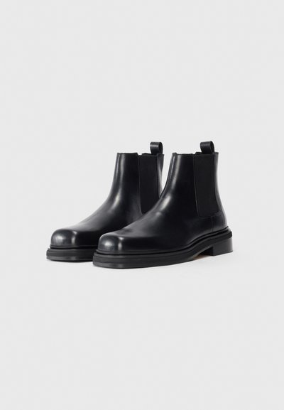 Black leather ankle boots with a smooth finish, elastic side panels, and pull tabs. Thick black rubber soles and rounded toe design.