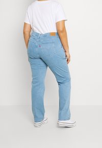 Jeans in denim azzurro chiaro con taglio dritto, caratterizzati da una patch sul retro color sabbia e due tasche posteriori. Abbinati a sneakers bianche.