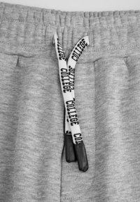 Szare dresy z pasem ściągającym, z nadrukiem "COLLEGE" i ciemnymi plastikowymi końcówkami sznurka. Materiał jest miękki i dziany, z elastyczną talią.