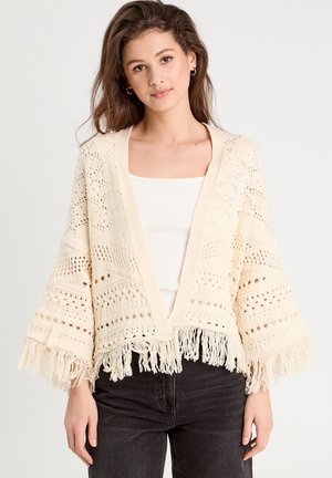 Cardigan en tricot crème, avec une ouverture sur le devant, des manches évasées et un ourlet à franges. Présente un motif texturé et un design aérien et ample.