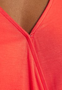 Tela roja con una textura suave y un diseño de escote en V. Presenta detalles de costura en el cuello y el hombro.