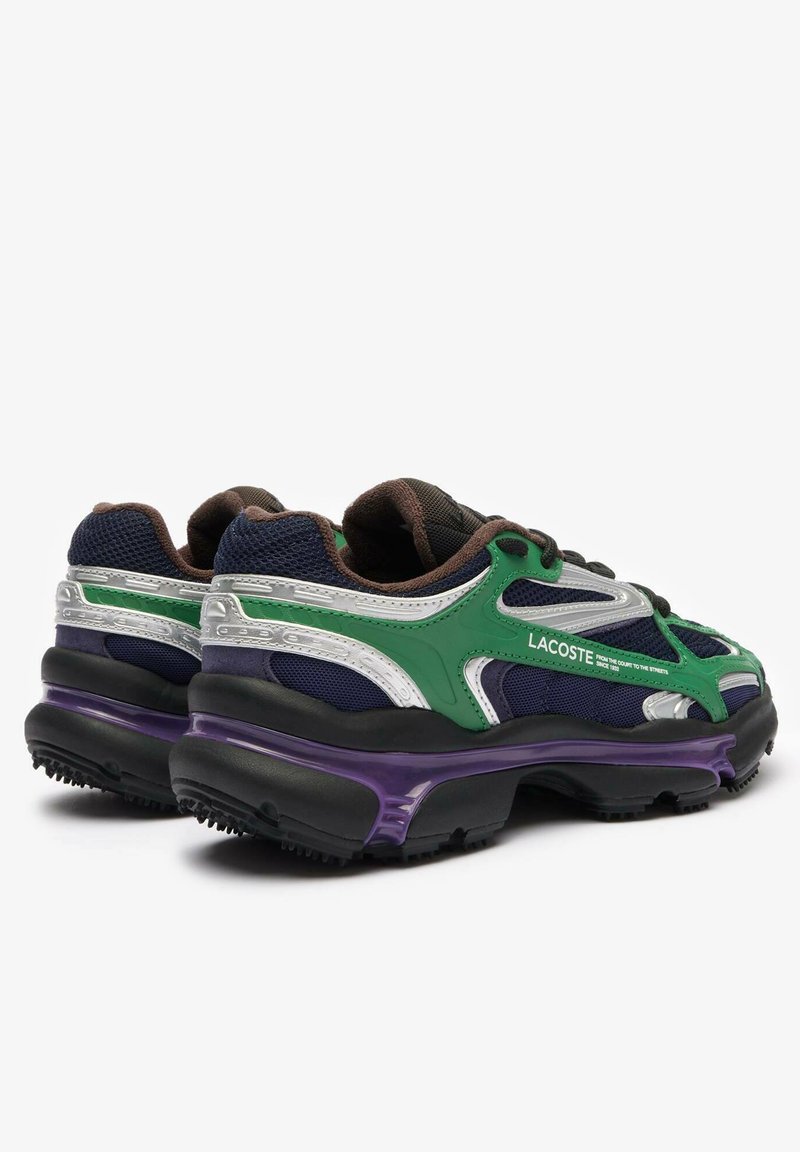 Baskets Lacoste avec une tige en mesh bleu marine et vert, accents argentés, et une semelle noire épaisse avec des détails violets. Présente un design à lacets.