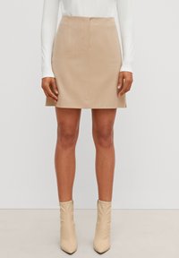 Mini-jupe beige à taille ajustée, avec des plis subtils et une texture lisse. Associée à des talons beiges montant jusqu'aux genoux.