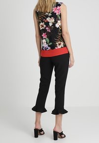 Top floreale senza maniche di colore nero con fiori colorati; vita rossa. Pantaloni neri cropped con orli a balze. Modella indossa sandali neri con tacco a blocco.