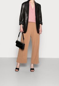 Blazer en cuir noir, pull en V rose, pantalon large beige, et sandales noires. Comprend un sac à main noir avec une chaîne dorée.