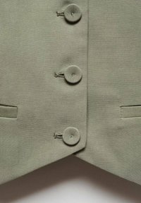 Gilet en tissu vert clair avec cinq boutons texturés et deux poches latérales, au design structuré, ajusté et aux bords nets.