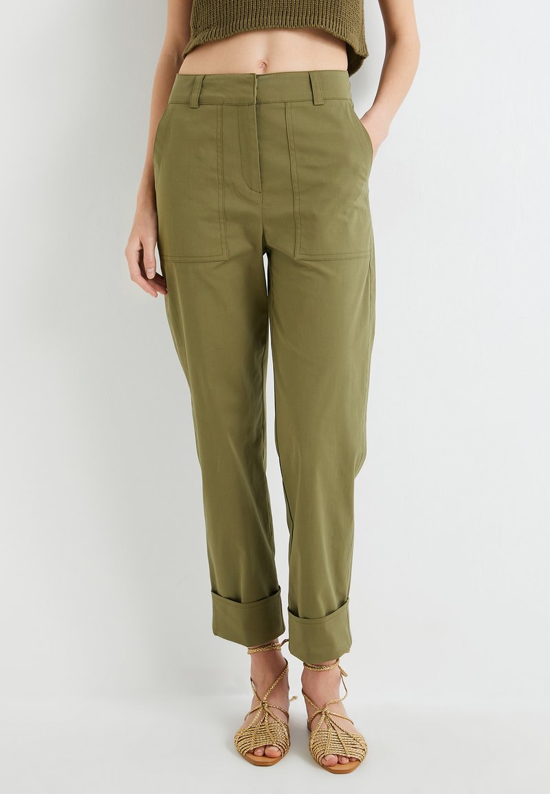 Pantalons vert olive avec des manches roulées, dotés de poches plates sur le devant et d'une texture lisse, associés à des sandales tressées à lanières.