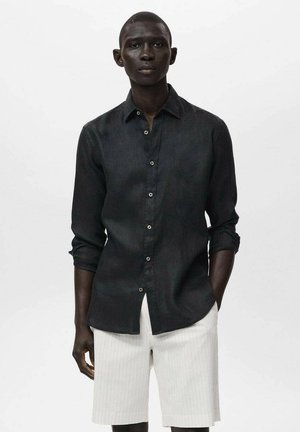 Camicia nera in lino con colletto, maniche lunghe e vestibilità rilassata, abbinata a pantaloni corti bianchi con texture.