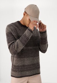 Pulover în dungi gri și maro din tricot, cu guler rotund. Complementat de o șapcă de baseball bej. Textură moale, croială lejeră.