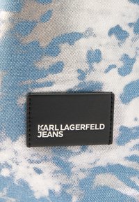 Sort rektangulært mærkat med teksten "KARL LAGERFELD JEANS" syet på blå og hvidt mønstret denimstof.