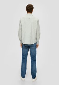 Gestreiftes Hemd mit Kragen aus leichtem Stoff, das vertikale grüne und blaue Streifen aufweist, kombiniert mit dunkelblauen Jeans und weißen Sneakers.