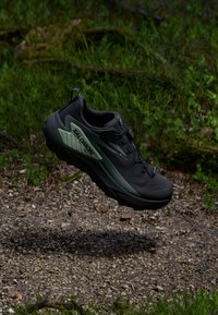 Chaussure de trail noire avec une accentuation verte, dotée d'une tige respirante, d'une semelle texturée et d'un logo bien visible sur le côté.