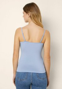 Top in morbido tessuto di cotone azzurro con spalline sottili e design aderente, indossato con jeans blu a vita alta.