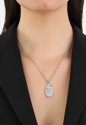 Collana d'argento con un pendente ovale, caratterizzata da una superficie texturizzata e dettagli a forma di perla, indossata su un indumento nero con colletto.