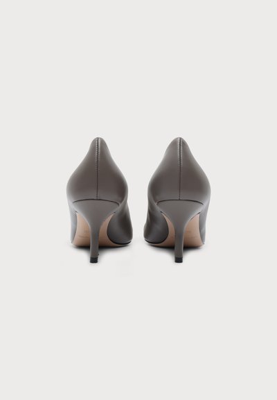 Paire d'escarpins en cuir brun à bout pointu vus de dos sur un fond clair uni.