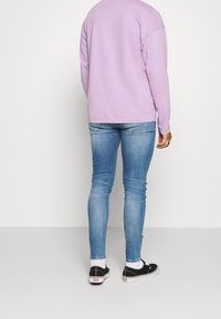 Camisa de manga larga color lavanda, jeans ajustados azul claro, zapatillas negras con suelas blancas. Material de algodón, diseño sencillo, sin patrones visibles.