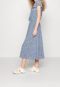 Blåblommig midikjol med korta volangärmar. Kombinerad med vita sneakers med beige detaljer och en strukturerad sula.