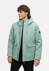 Chaqueta con capucha de color verde menta, hecha de un tejido suave, con dos bolsillos frontales, cierre de cremallera, cordones ajustables y un acento negro en la manga.