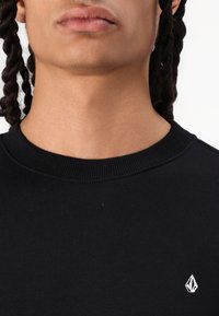 Schwarzer Rundhals-Sweatshirt aus Baumwolle. Verfügt über ein kleines weißes Logo auf der Brust und einen strukturierten Rippkragen.