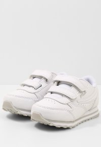 Scarpe sportive bianche con due cinturini in velcro, realizzate in materiale sintetico similpelle, con dettagli perforati e suola in gomma testurizzata. Logo Fila sul lato.
