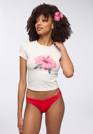 T-shirt bianco corto con un design floreale rosa, abbinato a pantaloni bikini rossi. Il tessuto morbido e le maniche corte esaltano il look casual.